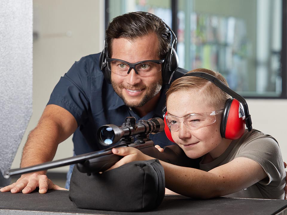 Firearms instructor helping kid fire a rifle